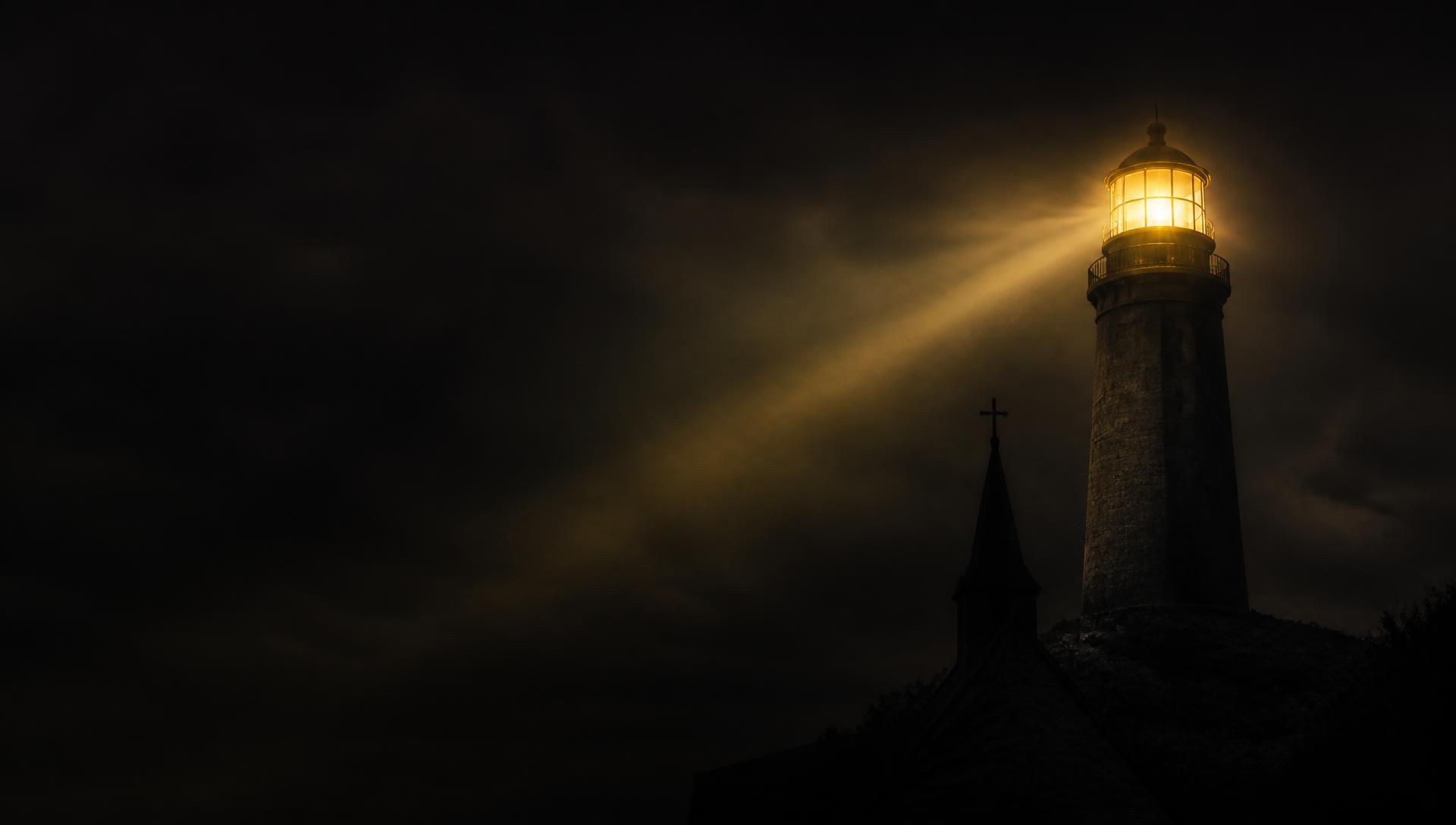 A lighthouse casting a golden beam over a church steeple at night